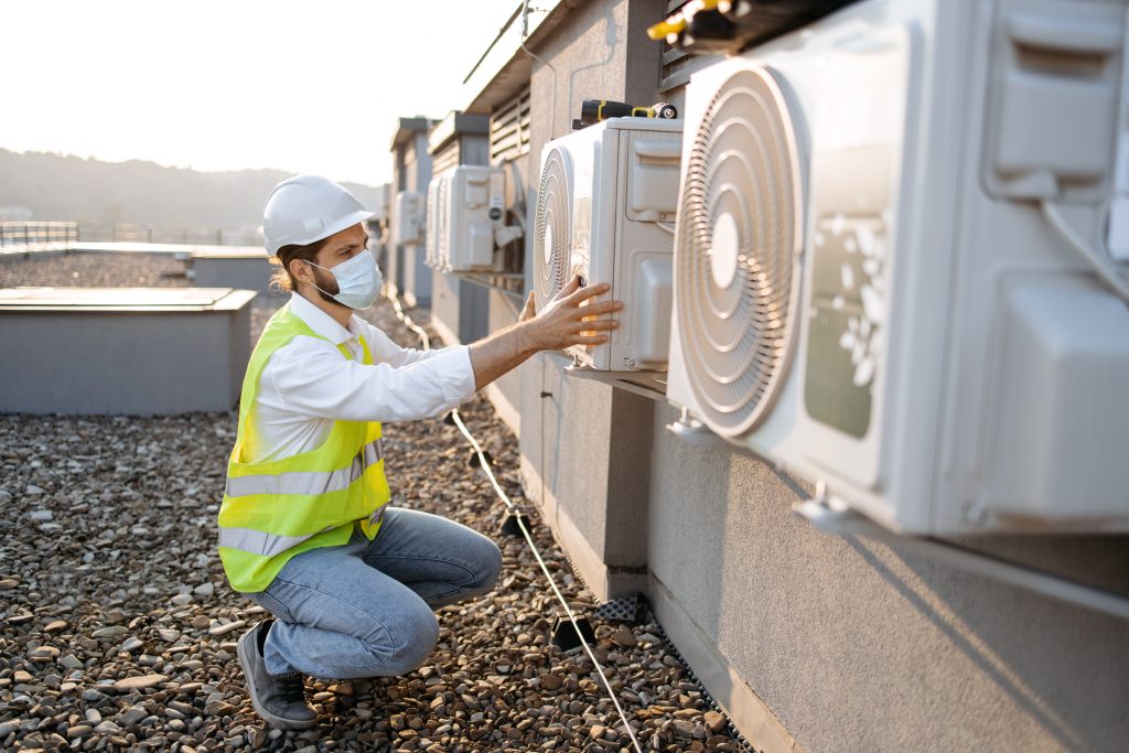 Homme inspectant les conduits de chauffage présents sur le toit d’un immeuble résidentiel.